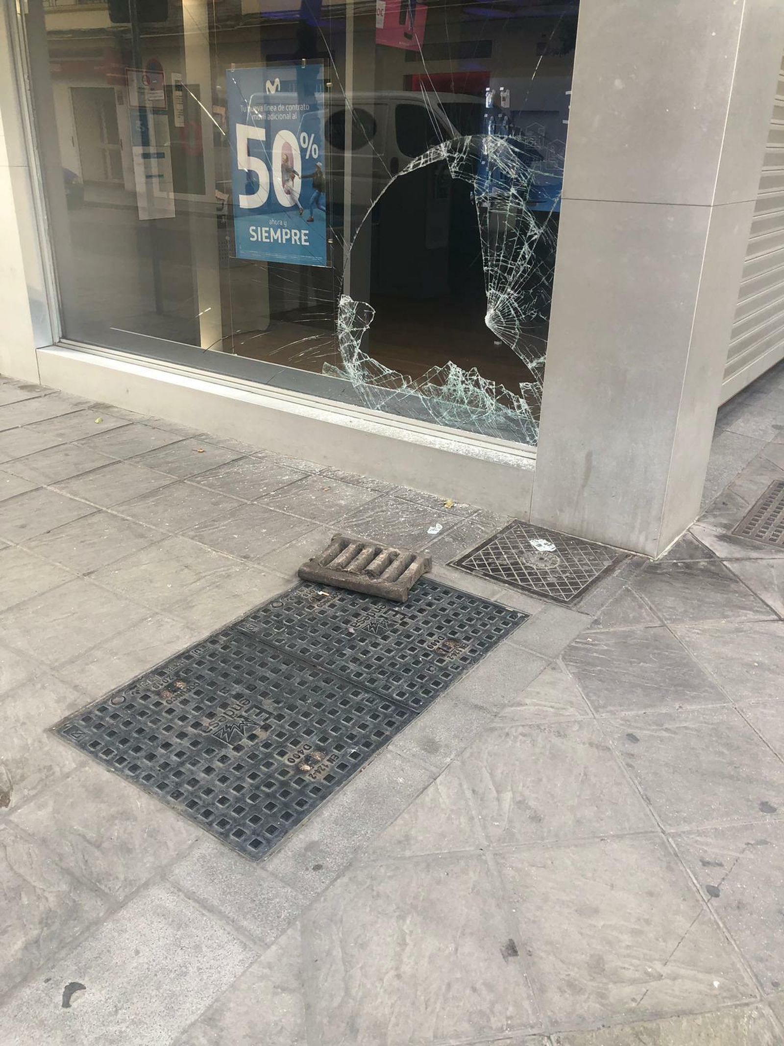La tapa de la alcantarilla junto al cristal de la tienda de Movistar