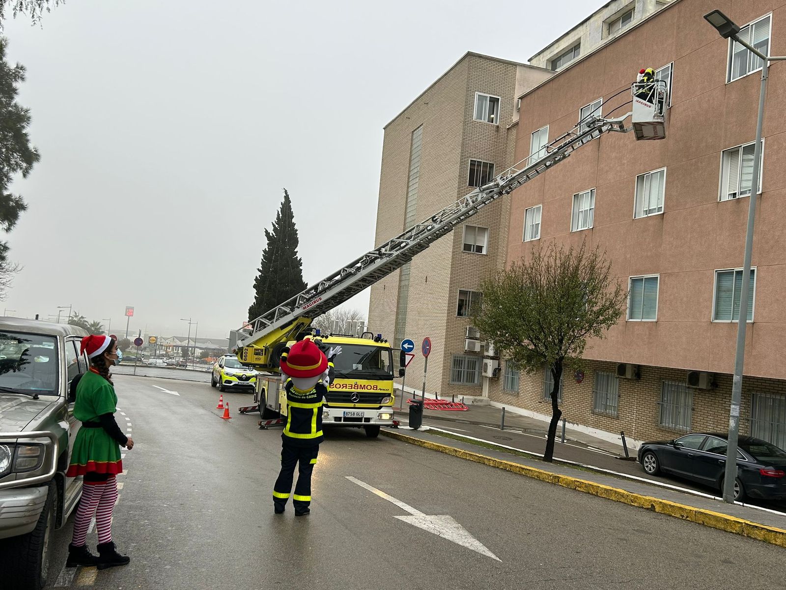 Bomberos ayudan a Papá Noel a alcanzar las ventanas del hospital para sorprender a los niños ingresados.