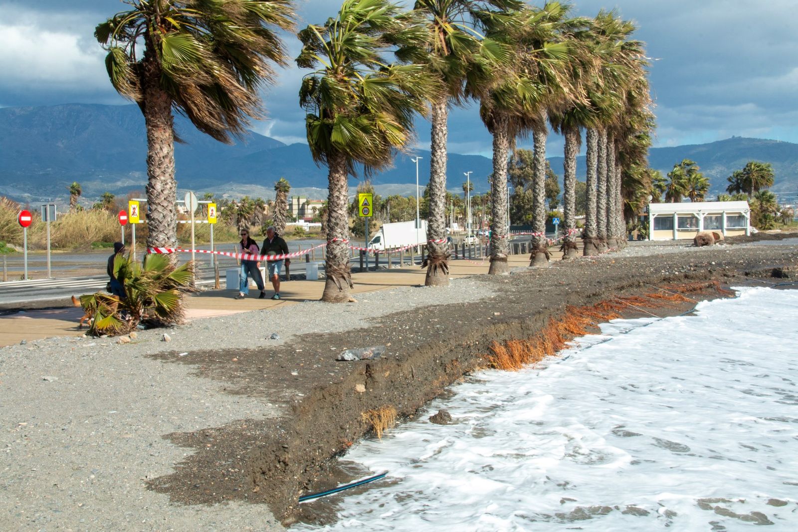 Unas personas pasean por la playa con el agua cerca de la Senda Litoral por el temporal