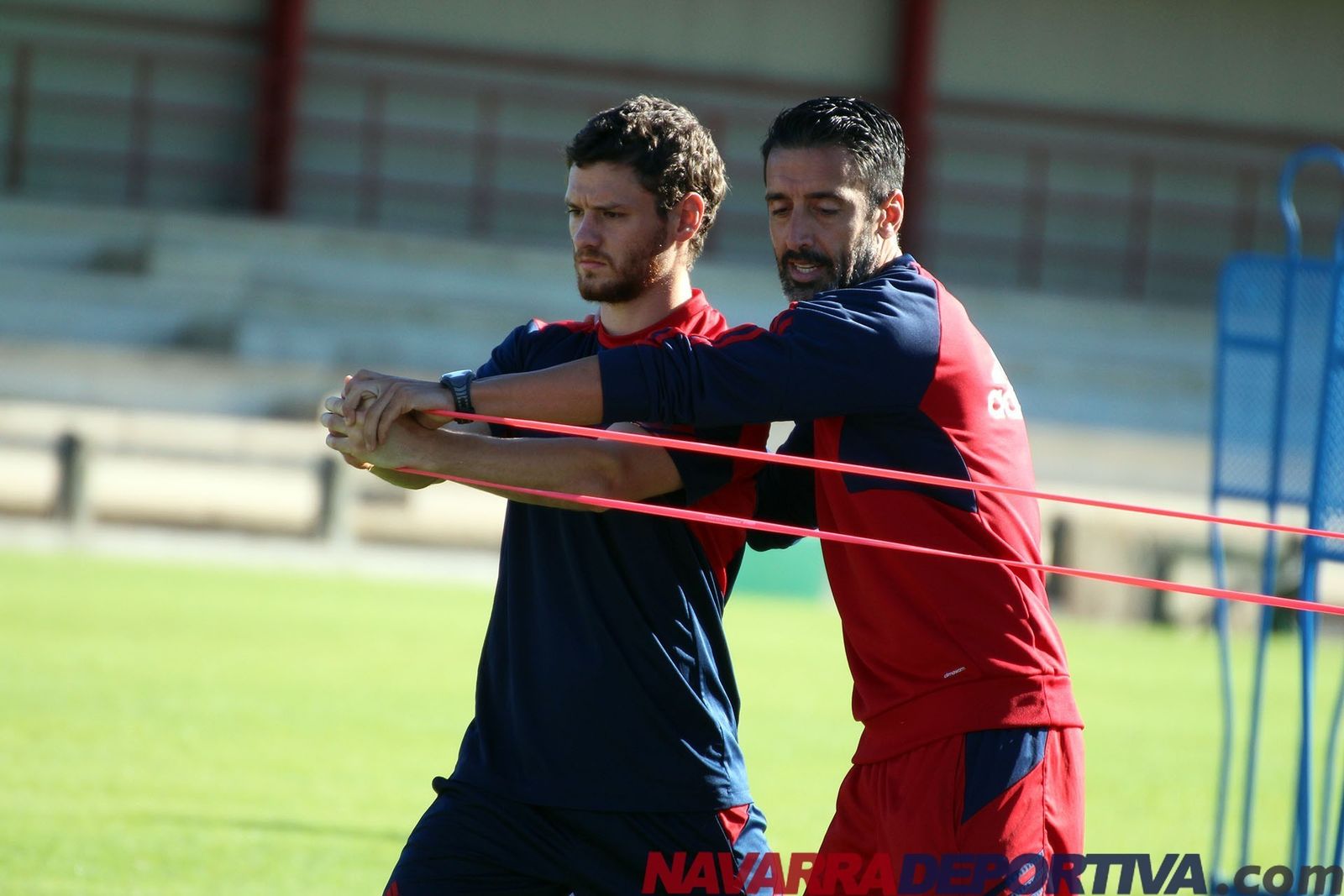 Pepe Conde (d) tira de un elástico para ayudar en un ejercicio al centrocampista osasunista Arzura.