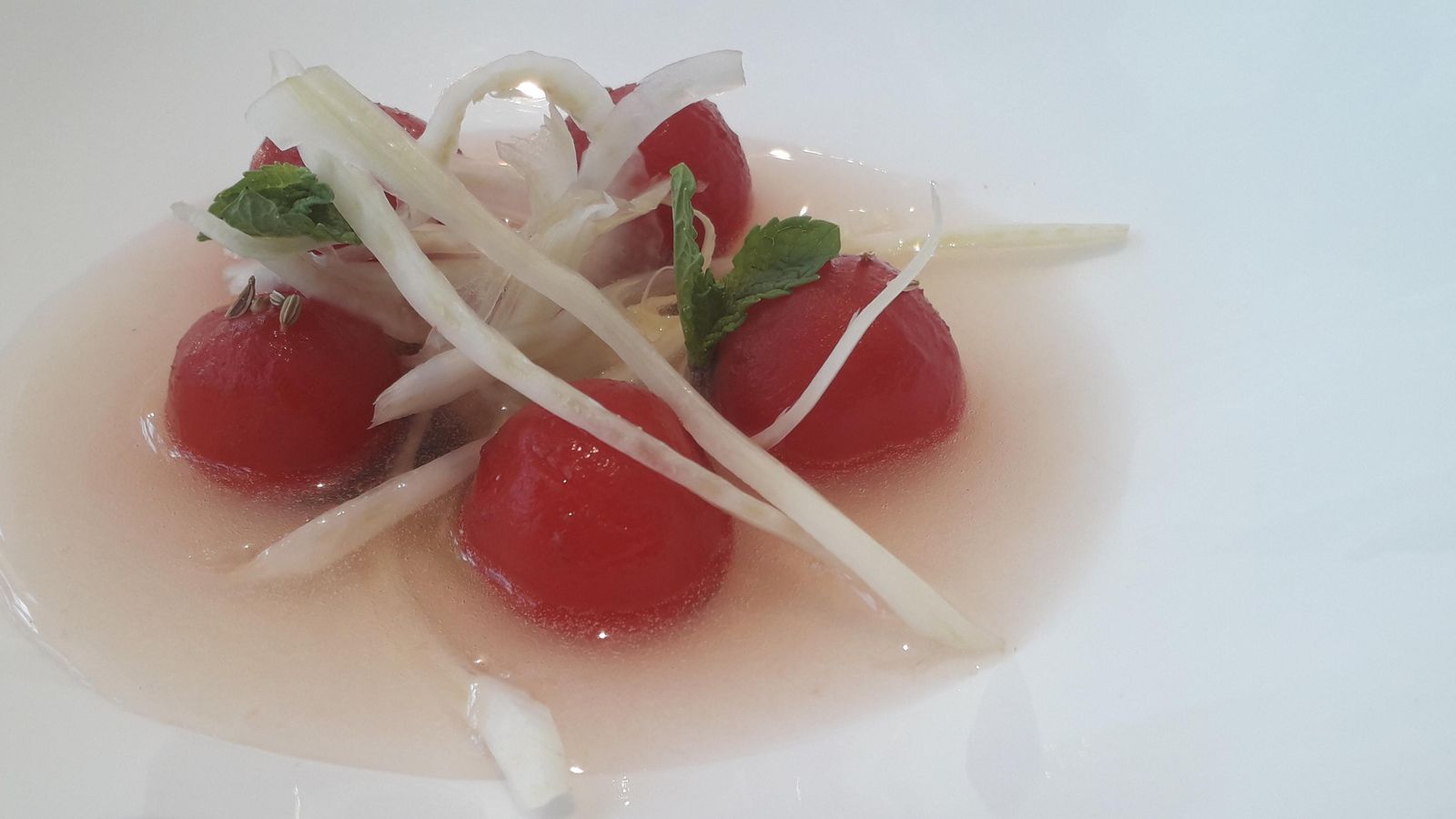 Ensalada de tomates servidos en su propia agua con hinojo y emulsión de aceituna y cilantro.