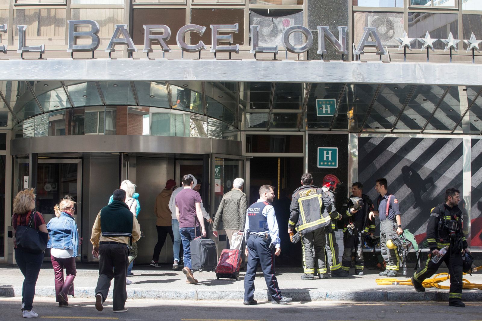 Varios bomberos y residentes del hotel, en la puerta del Expo Barcelona, tras ser desalojado por un incendio.