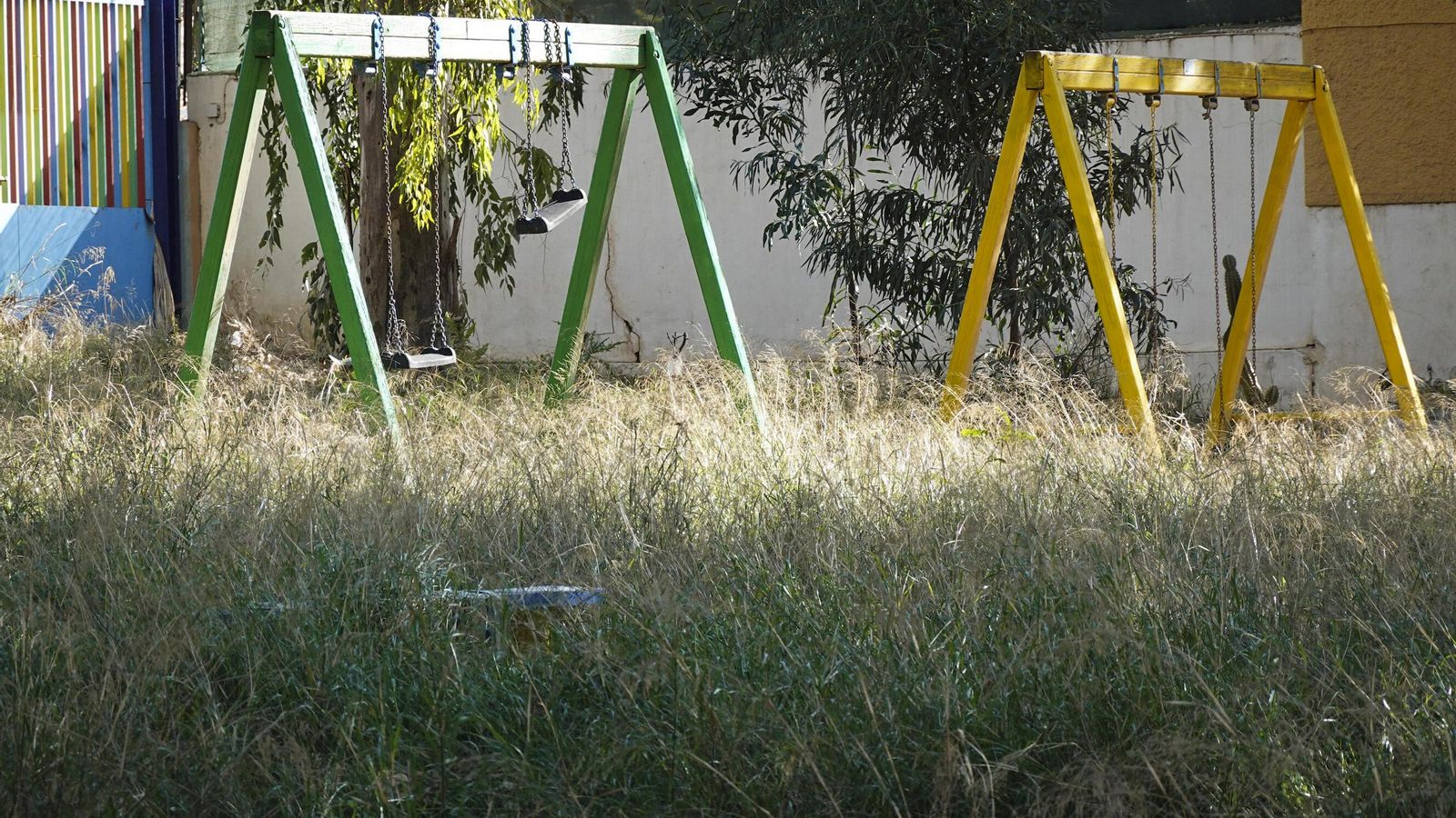 Columpios en uno de los patios de recreo, lleno de maleza.