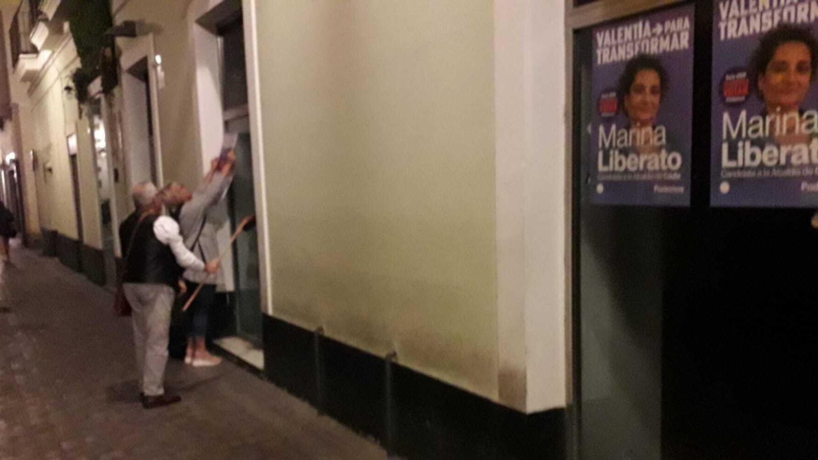 Pegando carteles de Marina Liberato (Podemos) en un escaparate de una tienda vacía.