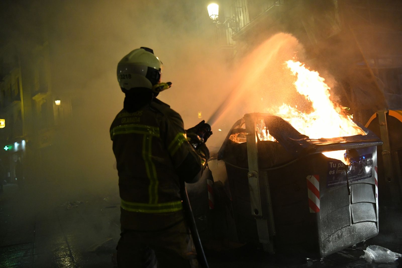 Un bombero extingue uno de los contenedores quemados