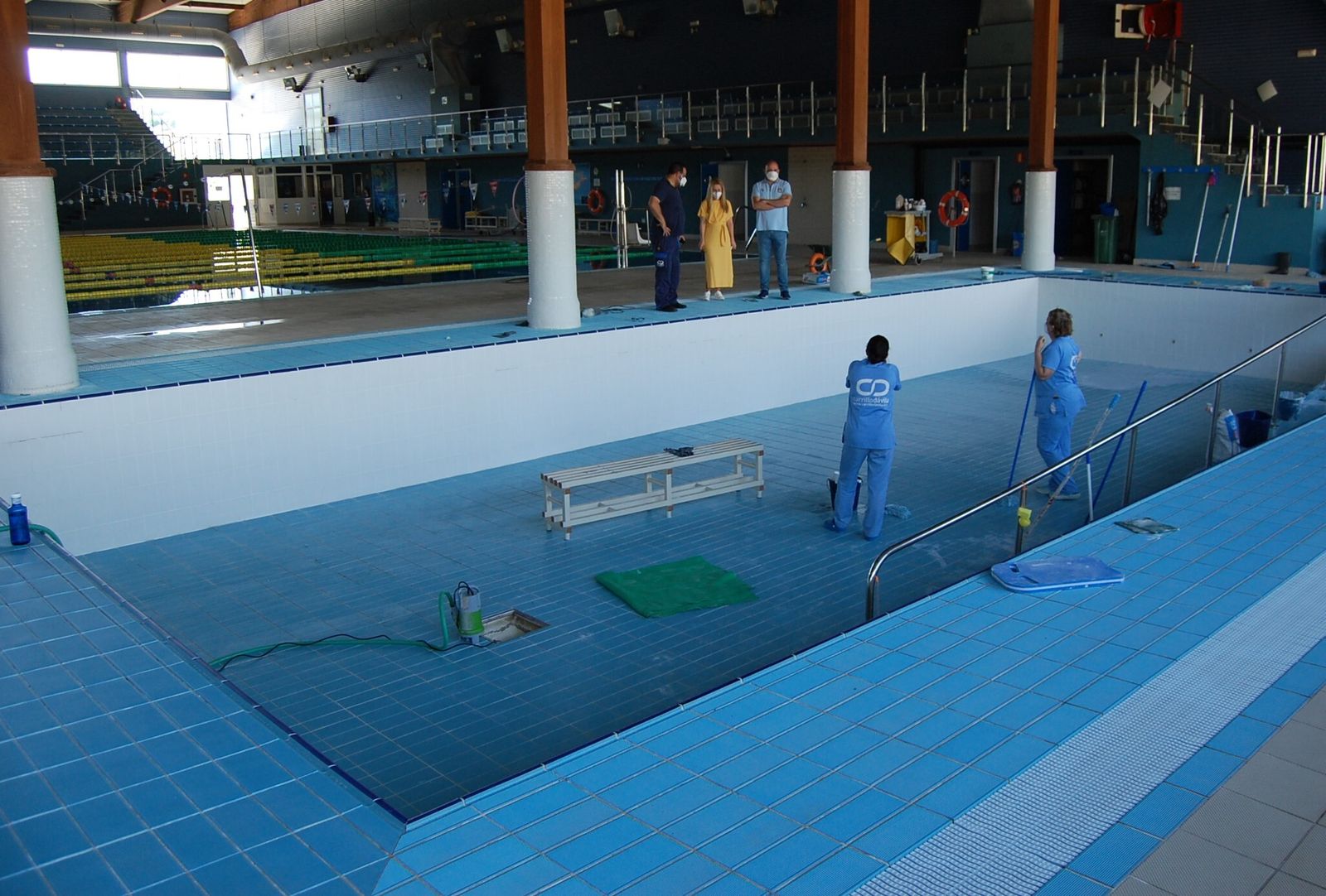 Dos personas efectúan una limpieza a fondo de uno de los vasos de la piscina cubierta.