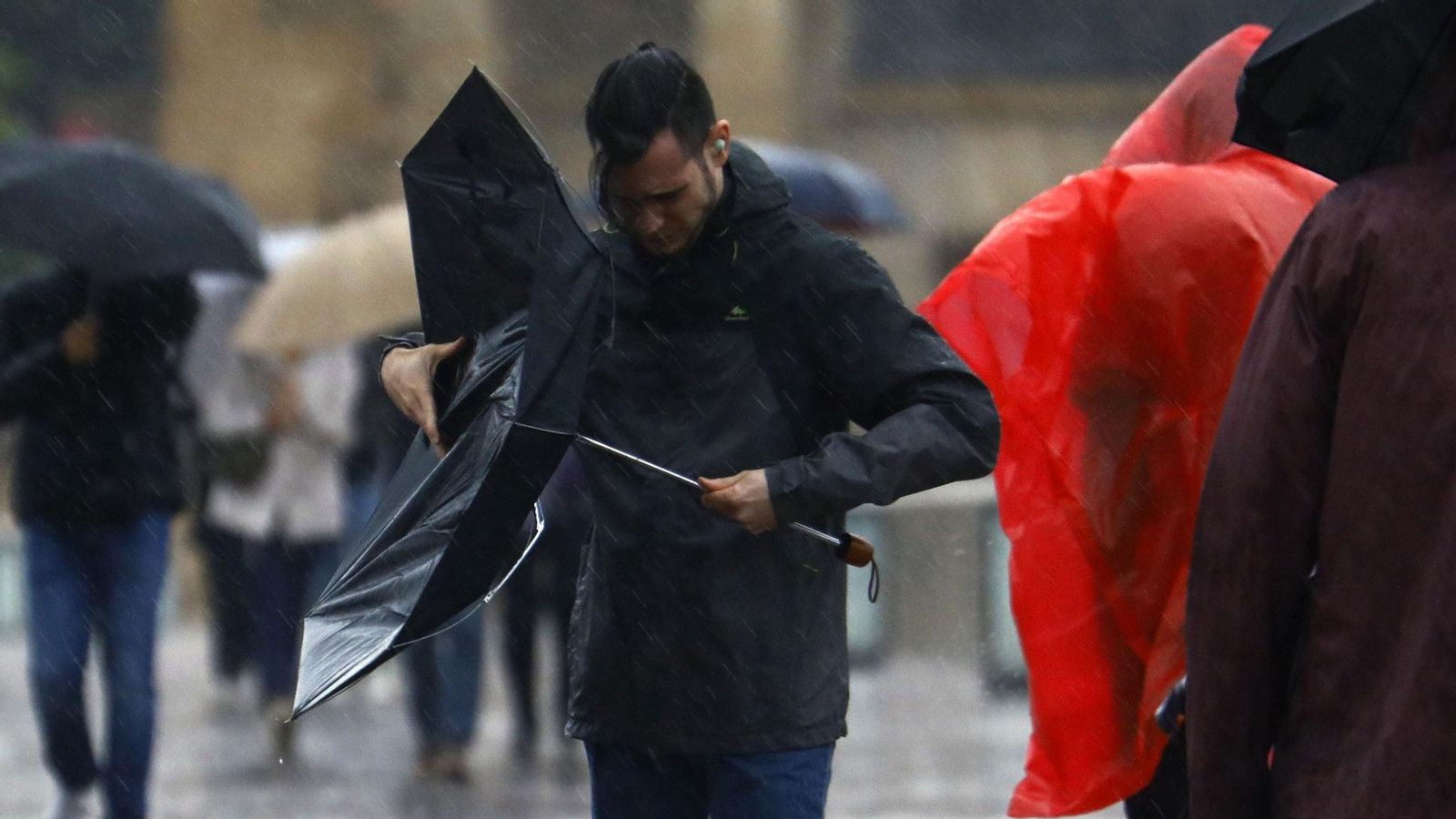 Un hombre intenta arreglar un paraguas roto por el viento.