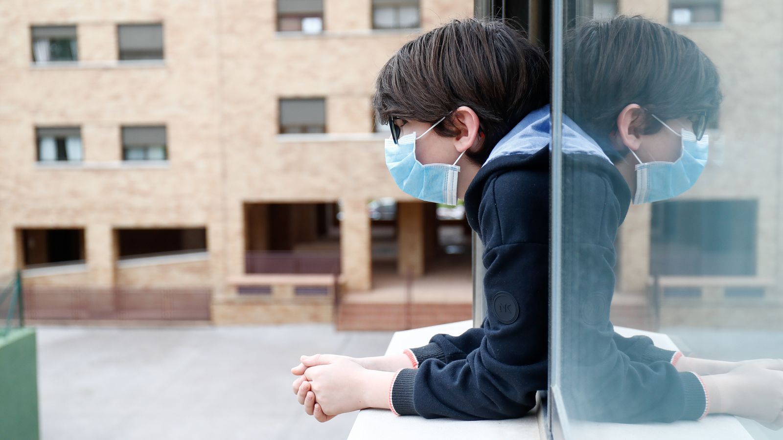 Un niño observa por la ventana con su mascarilla.