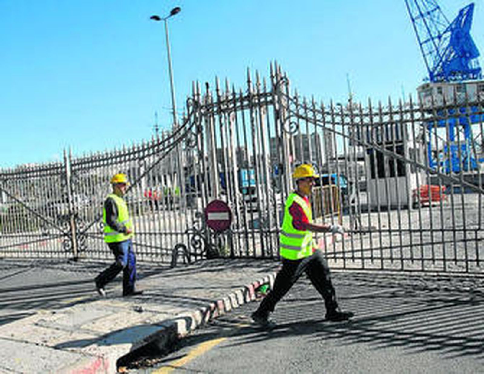 Dos obreros pasan junto a la puerta del puerto, frente a La Marina.