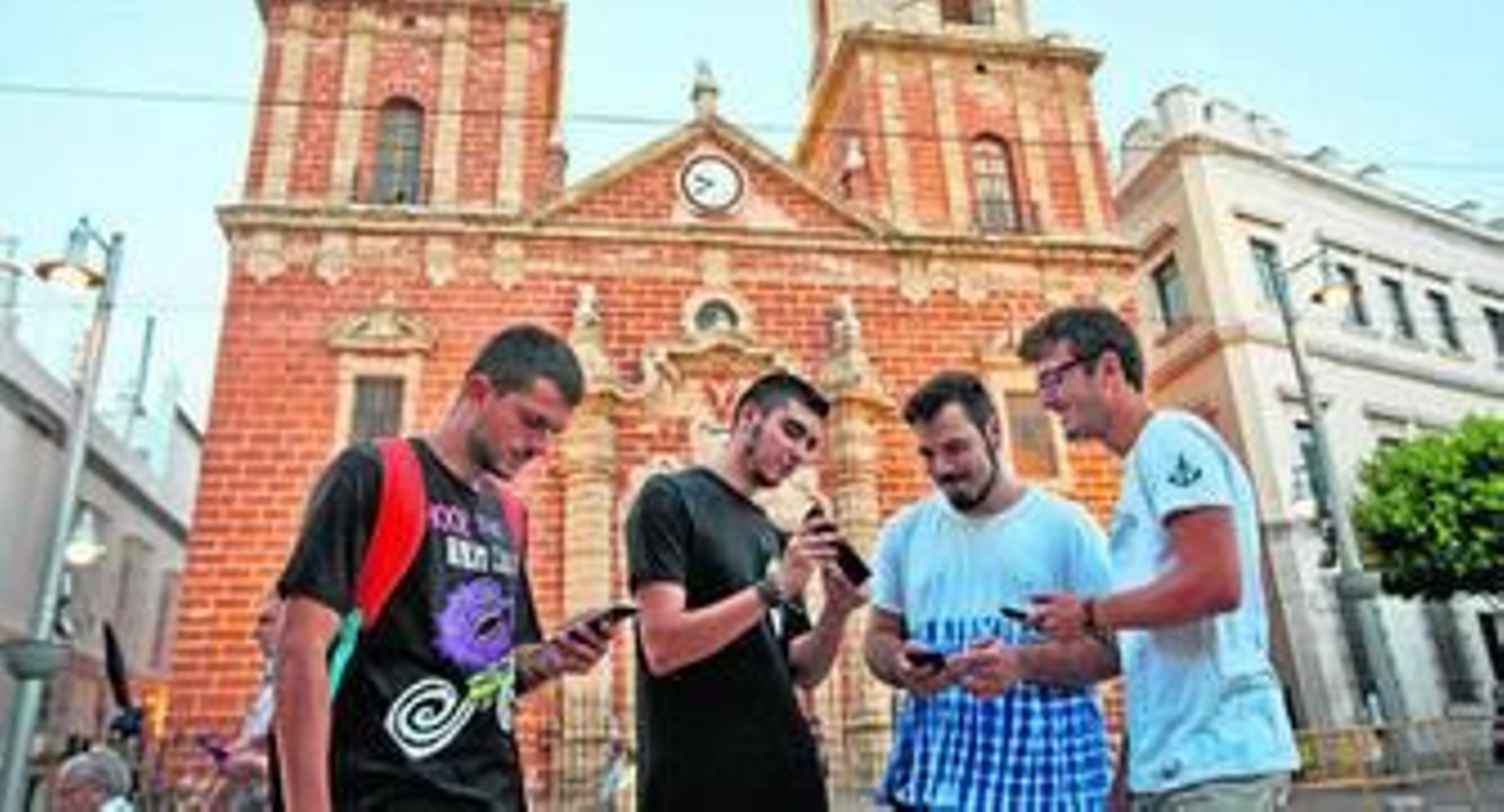 Varios jóvenes juegan con sus teléfonos móviles a Pokémon Go frente a la Iglesia Mayor.