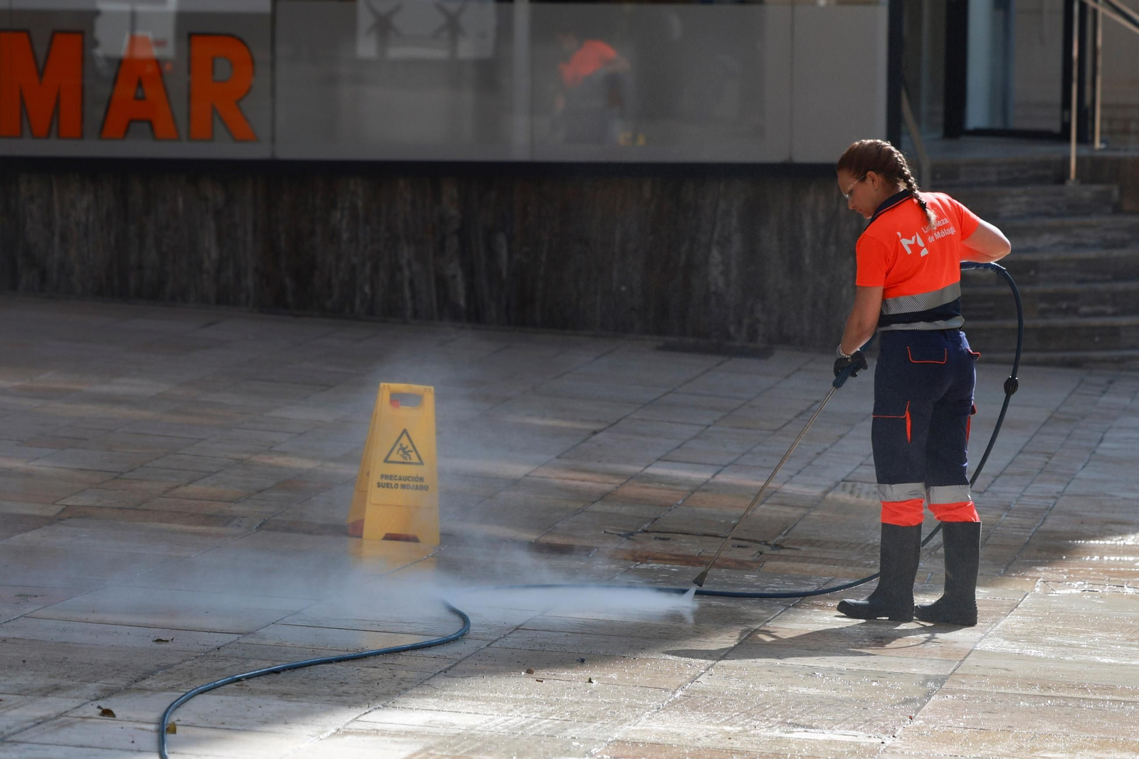 Una operaria baldeando una calle.