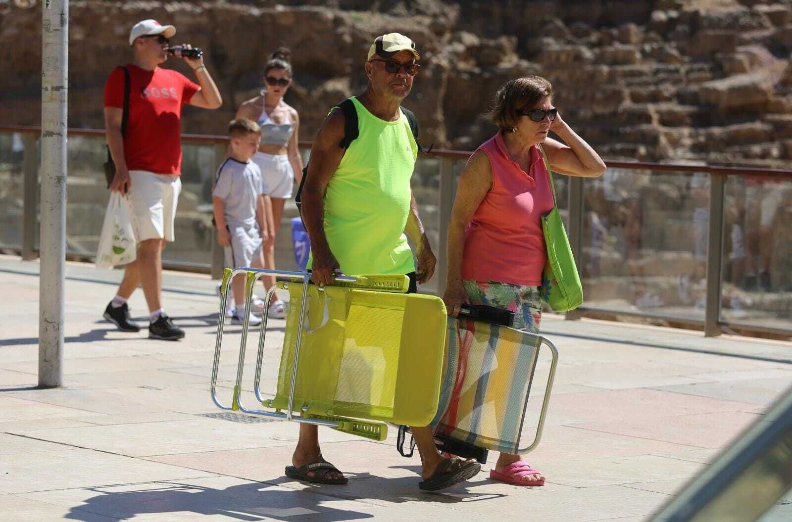 Dos personas con las sillas de la playa pasan por la calle Alcazabilla este martes.