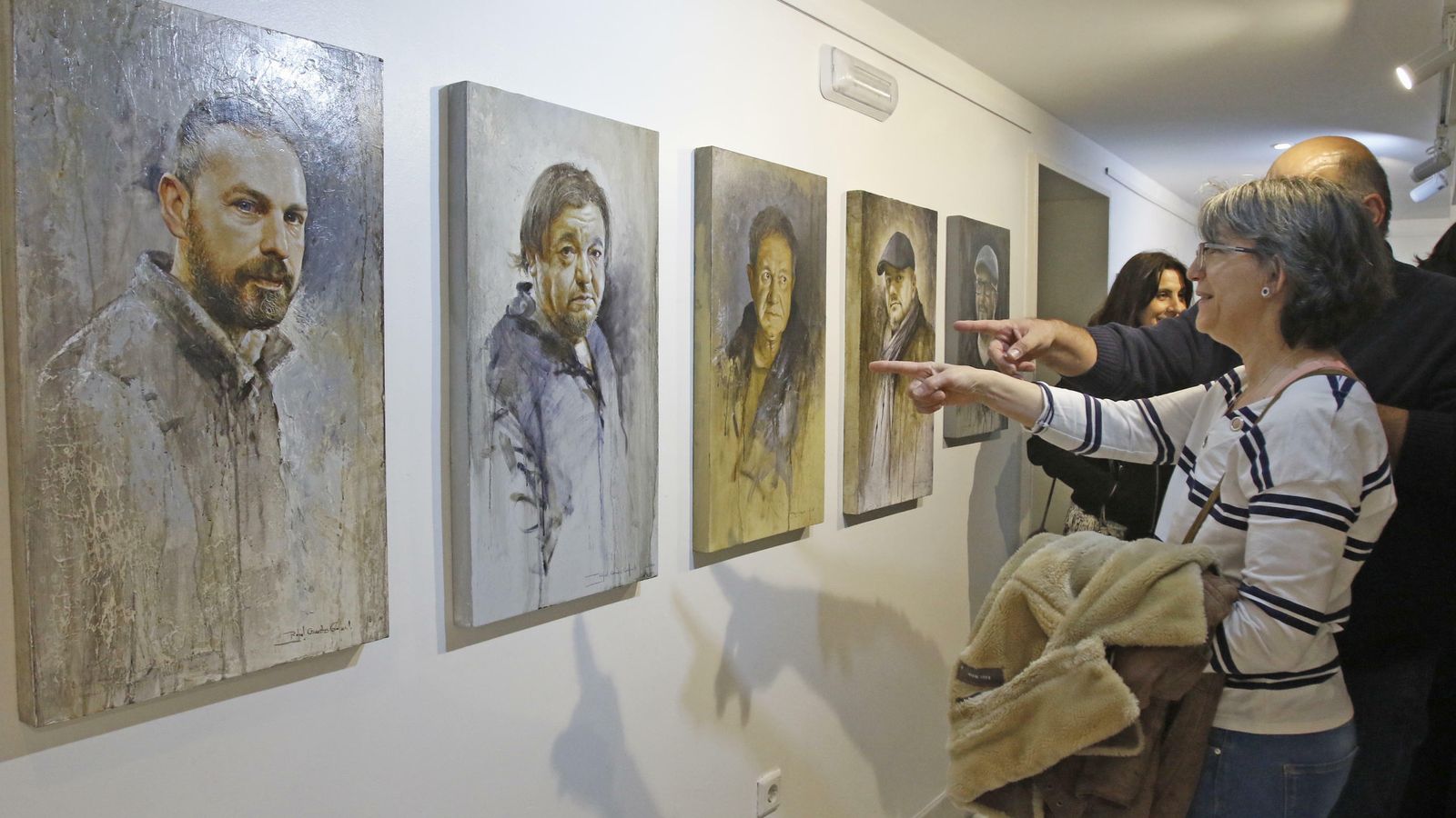 Dos personas señalan una de los retratos de la exposición.