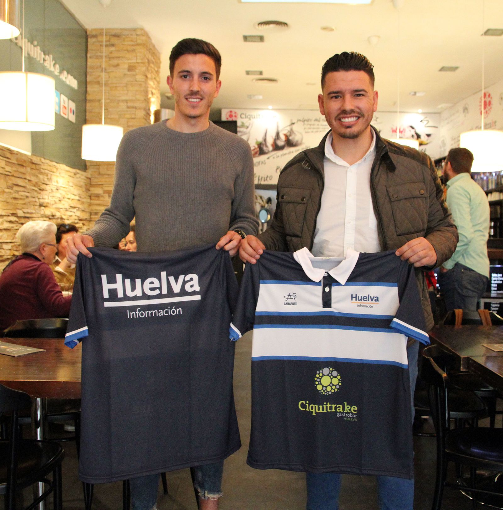 Alberto Ródenas y Joaquín Rasco posan con los polos de la Tertulia Deportiva de Huelva Información.