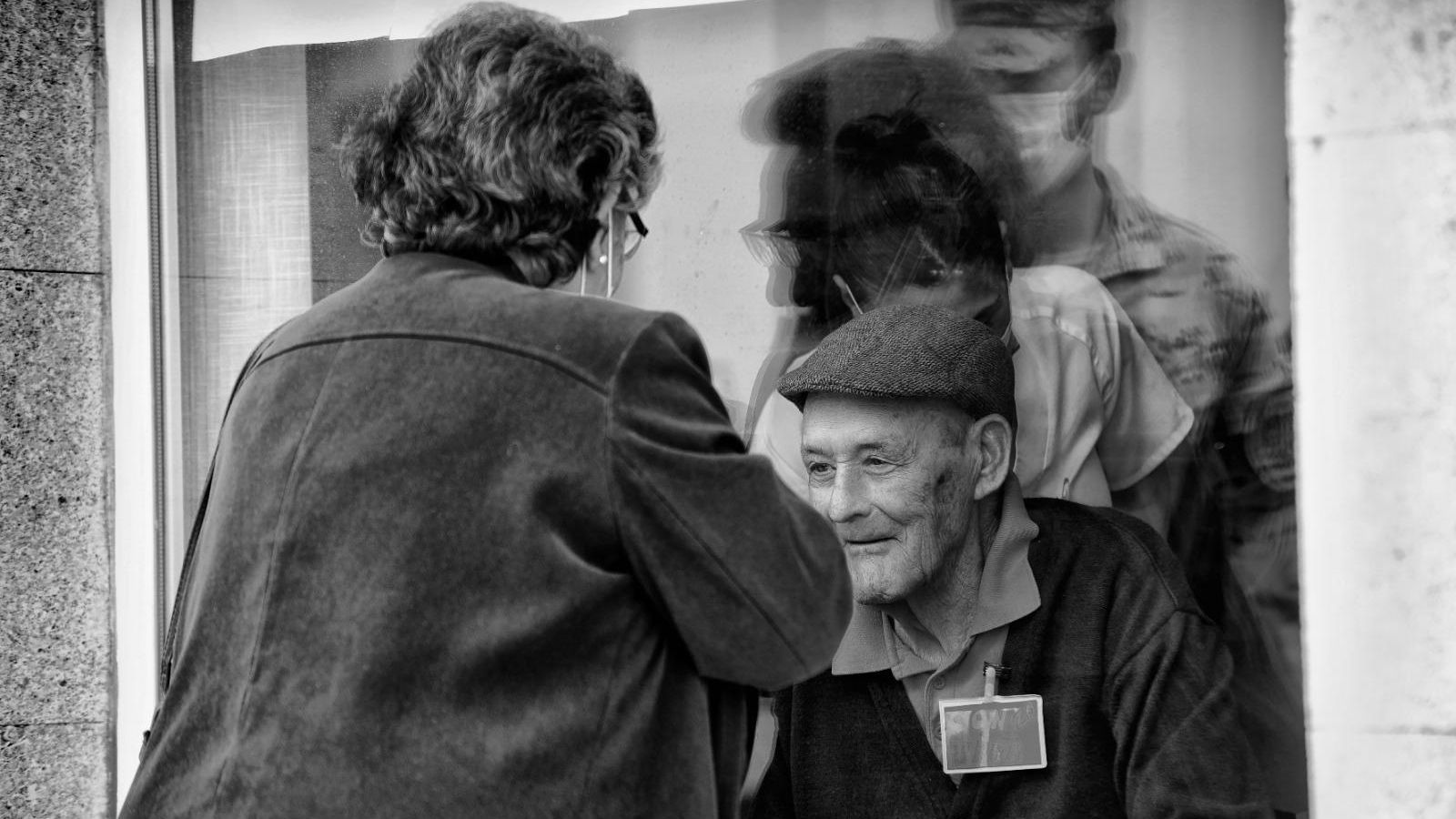 Familiares de residentes de Vedruna saludan a un anciano tras la ventana.