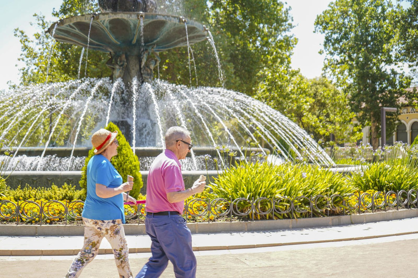 Dos ciudadanos caminan bajo un sol de justicia junto a la fuente de las Granadas mientras toman un helado