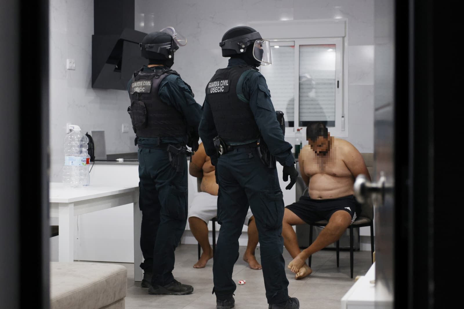 Los agentes, custodiando a los detenidos en el salón de la vivienda.