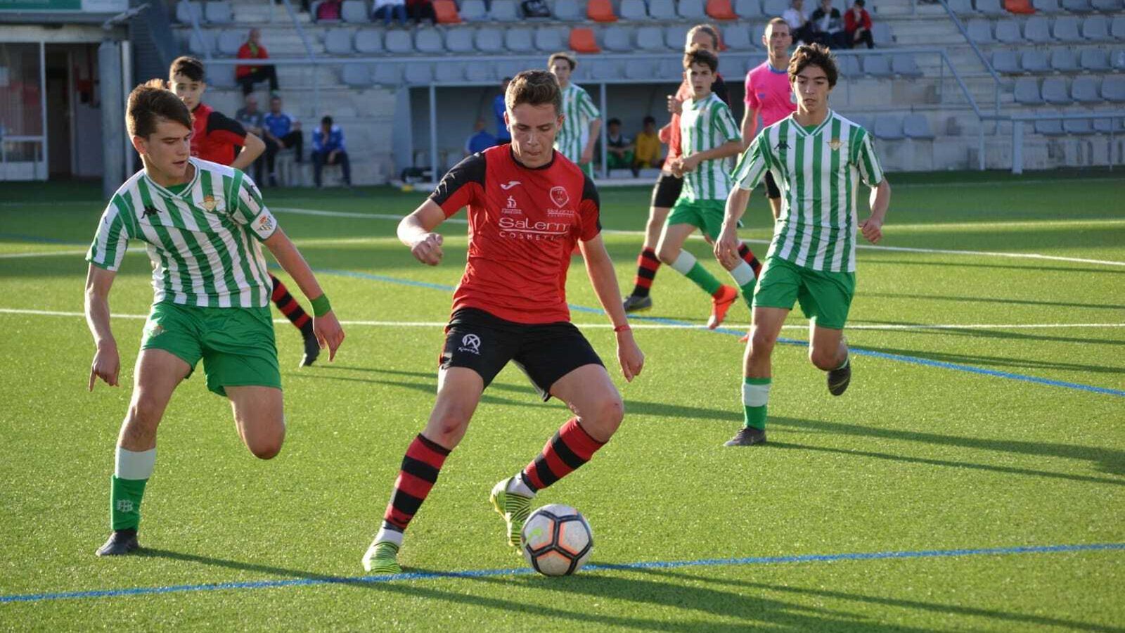 Un jugador del Salerm Puente Genil se lleva el balón ante la presión de un bético.