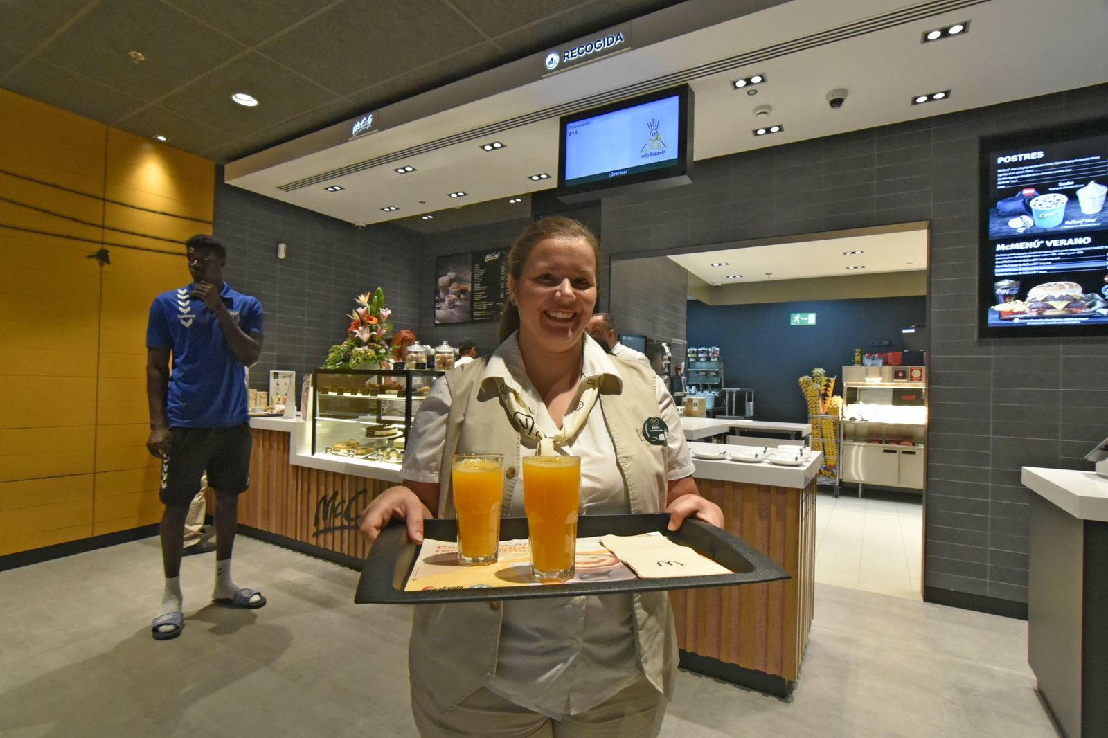 Una empleada de McDonald's porta una bandeja con dos zumos de naranja.