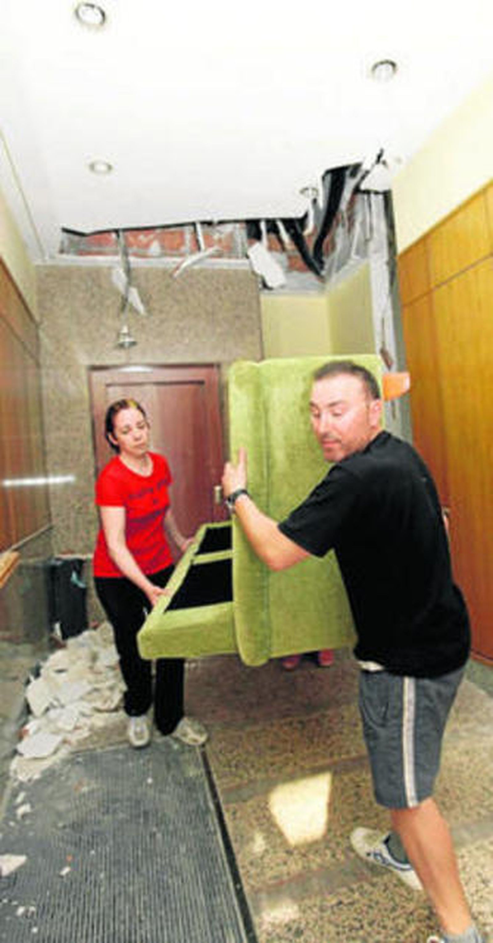 Dos vecinos rescatan un sofá de su casa entre escombros.