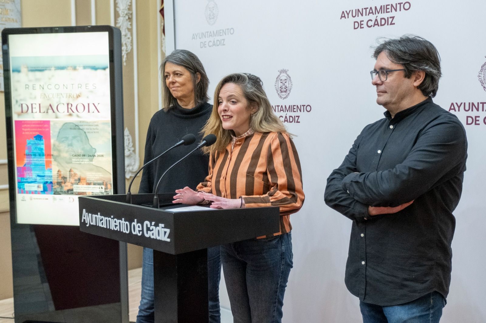 Karine Grossman, Maite González y Cecilio Chaves, ante el cartel anunciador de la exposición.