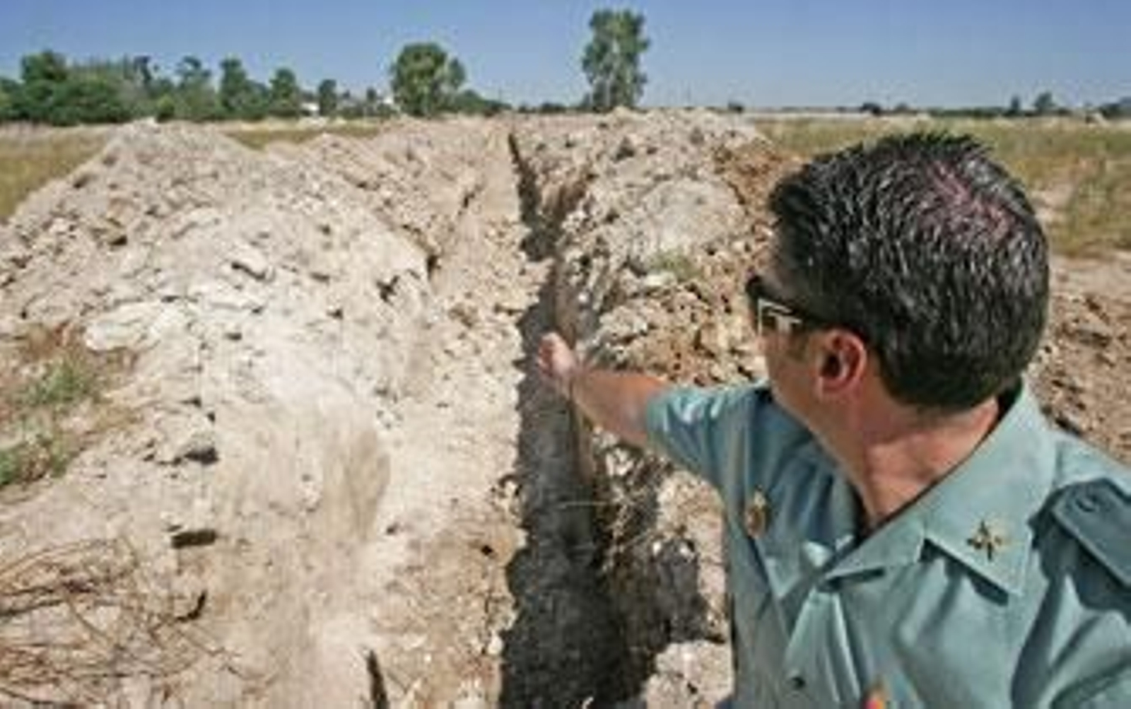 Un guardia civil señala la zanja donde unos ladrones expoliaron tuberías metálicas de la azucarera de Guadalcacín./Pascual