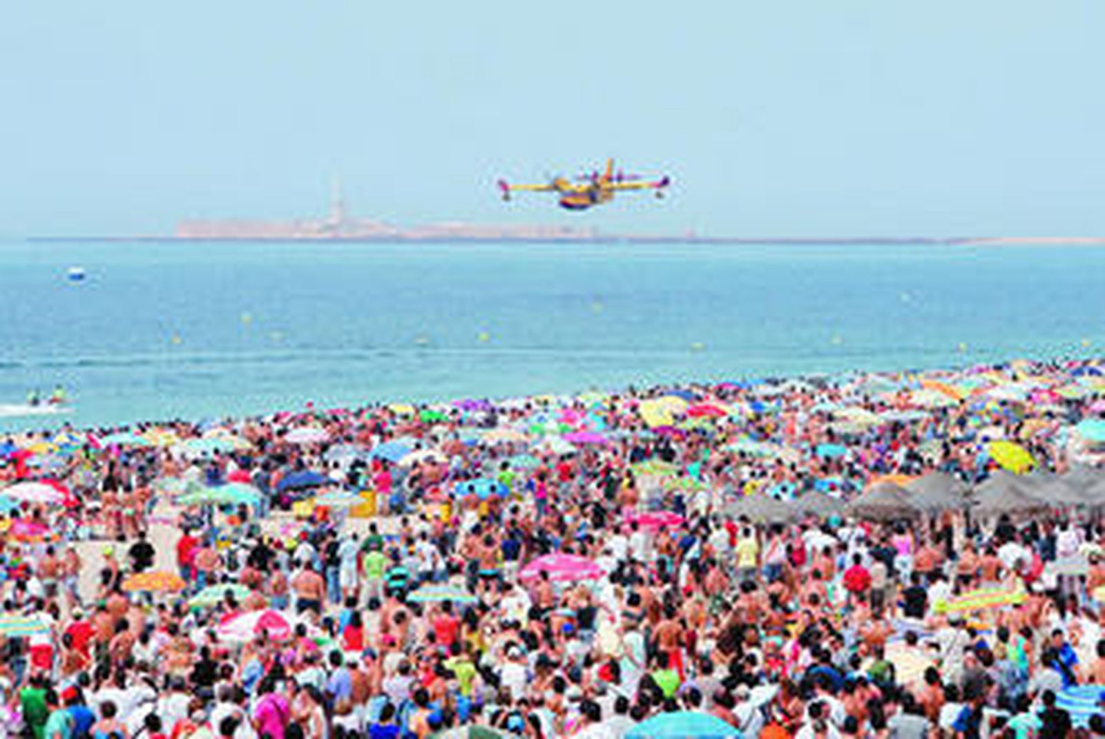 Un hidroavión vuela a baja altura en la playa Victoria ante centenares de personas.
