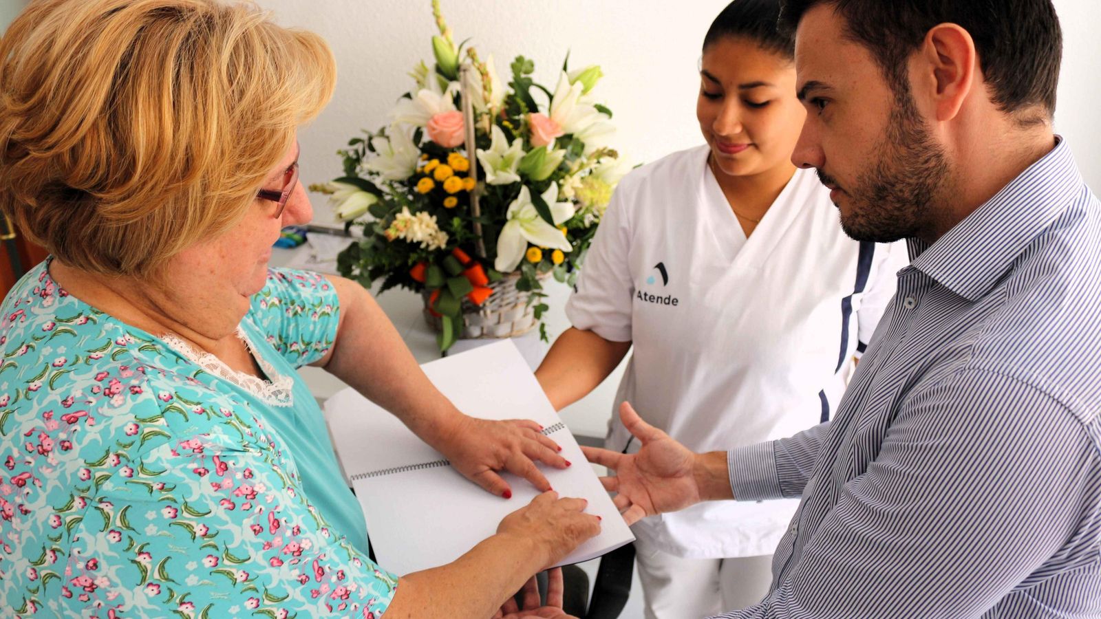 Isabel Mª Sánchez, usuaria, recibe de manos de Óscar Bleda, concejal Ayuntamiento de Almería, el manual en presencia de Génesis Holguin, auxiliar de Ayuda a Domicilio de Atende.