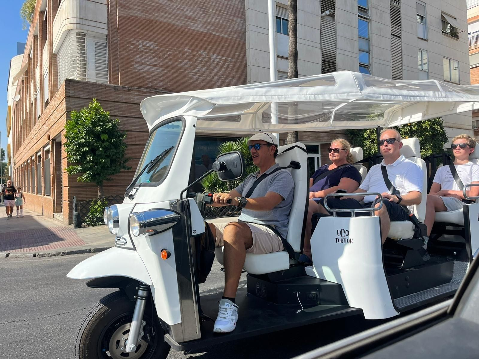 Un vehículo eléctrico tuk tuk realiza un recorrido por Sevilla con varios turistas.