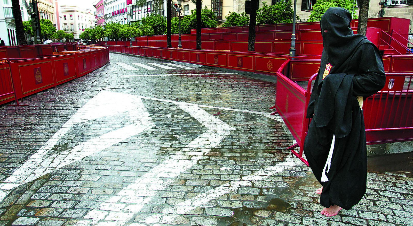 Un penitente de las Tres Caídas intenta cruzar la calle con charcos.