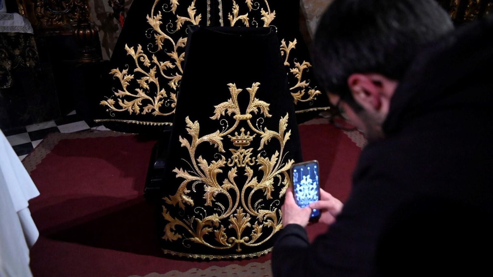 Un hermano de la hermandad fotografía la saya y el manto de la Virgen.