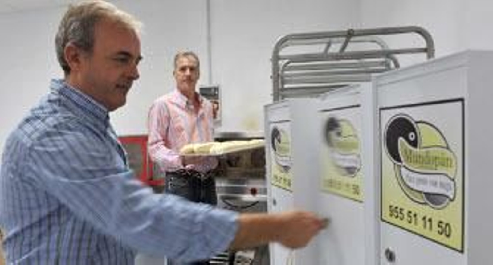 Ignacio Lagares abre un buzón-panera, mientras al fondo Lucas Burgos, su socio de Mundopán, prepara los panes. / Juan Carlos Vázquez