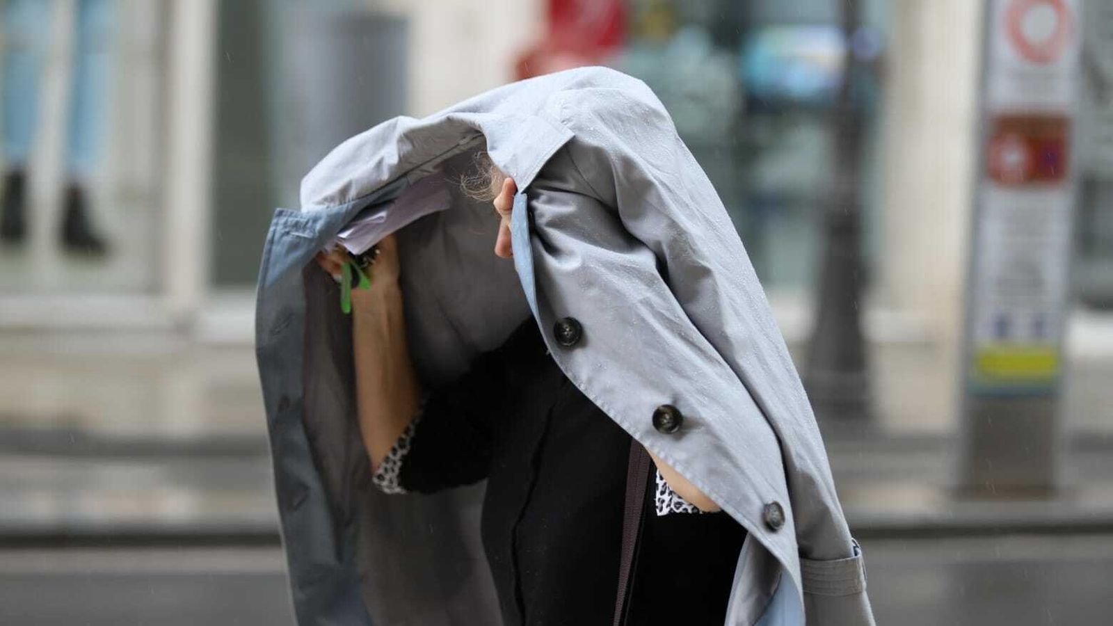 Una mujer se protege de la lluvia en Málaga con su abrigo.