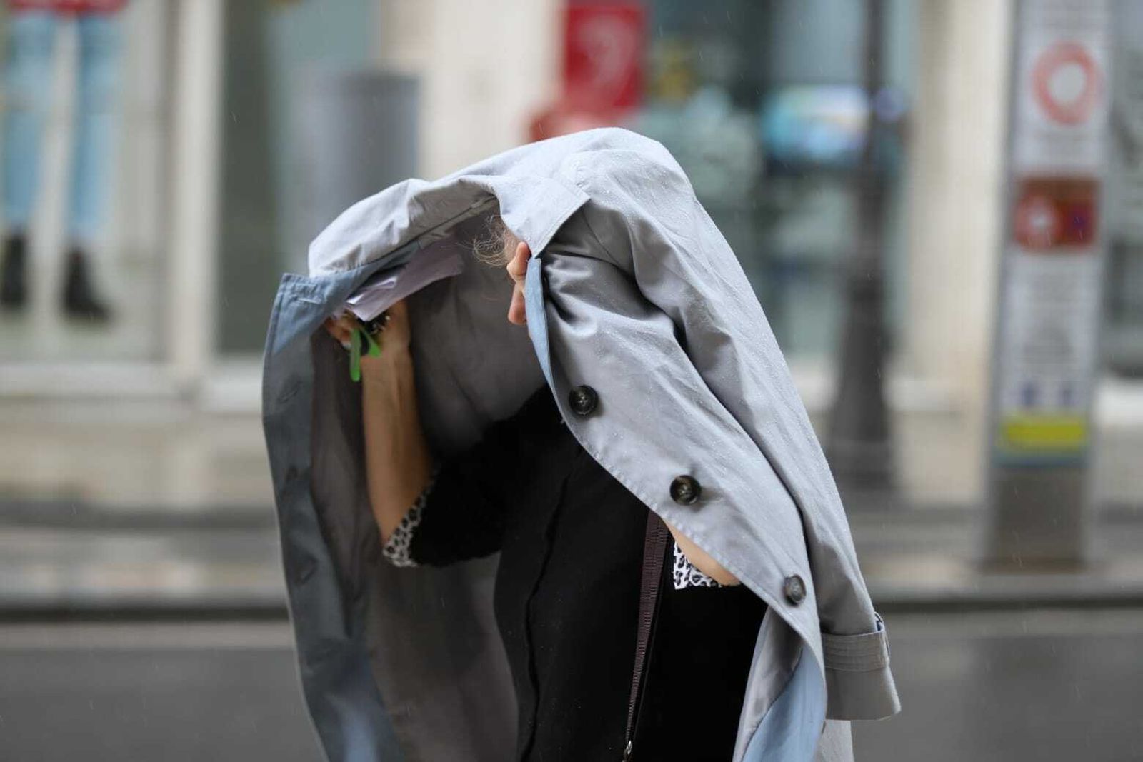 Una mujer se protege de la lluvia en Málaga con su abrigo.