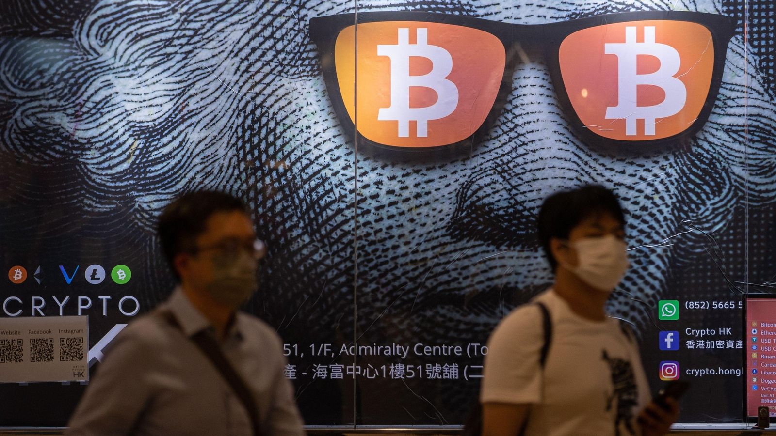 Dos hombres pasan junto a un cartel publicitario de Bitcoins y criptomonedas  en Hong Kong, China, el 25 de septiembre de 2021.