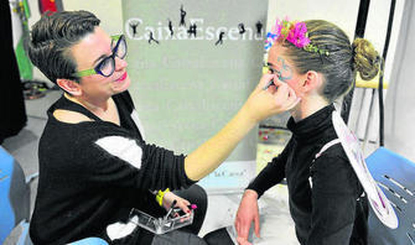 Una mujer pinta a una niña antes de comenzar el acto.