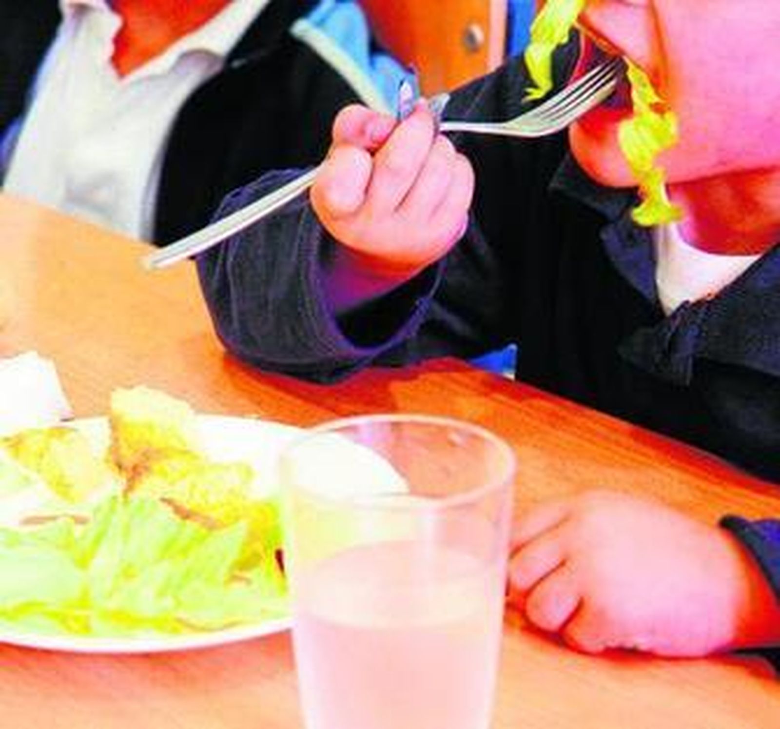 Niños comiendo ensalada en un comedor escolar.