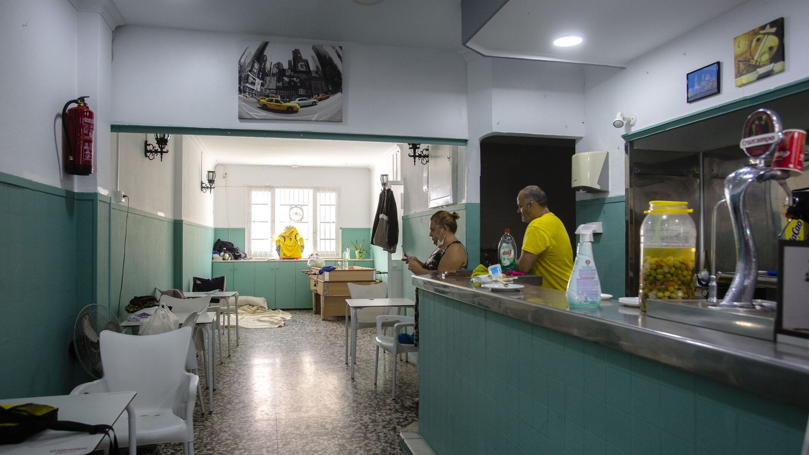 La barra y las mesas y sillas que hacen de sala y comedor. Al fondo, el improvisado dormitorio.