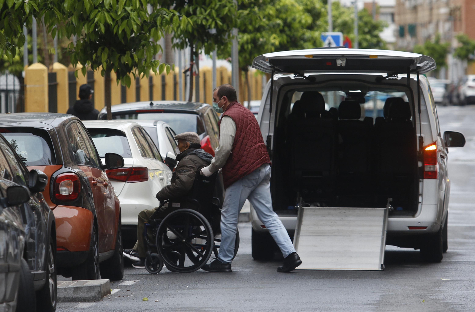 Un hombre saca de un coche a una persona mayor en silla de ruedas.