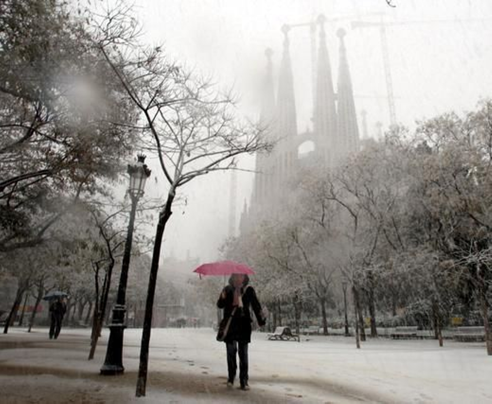 Una persona camina bajo la nieve con la Sagrada Familia de fondo. / EFE · AFP Photo · Reuters