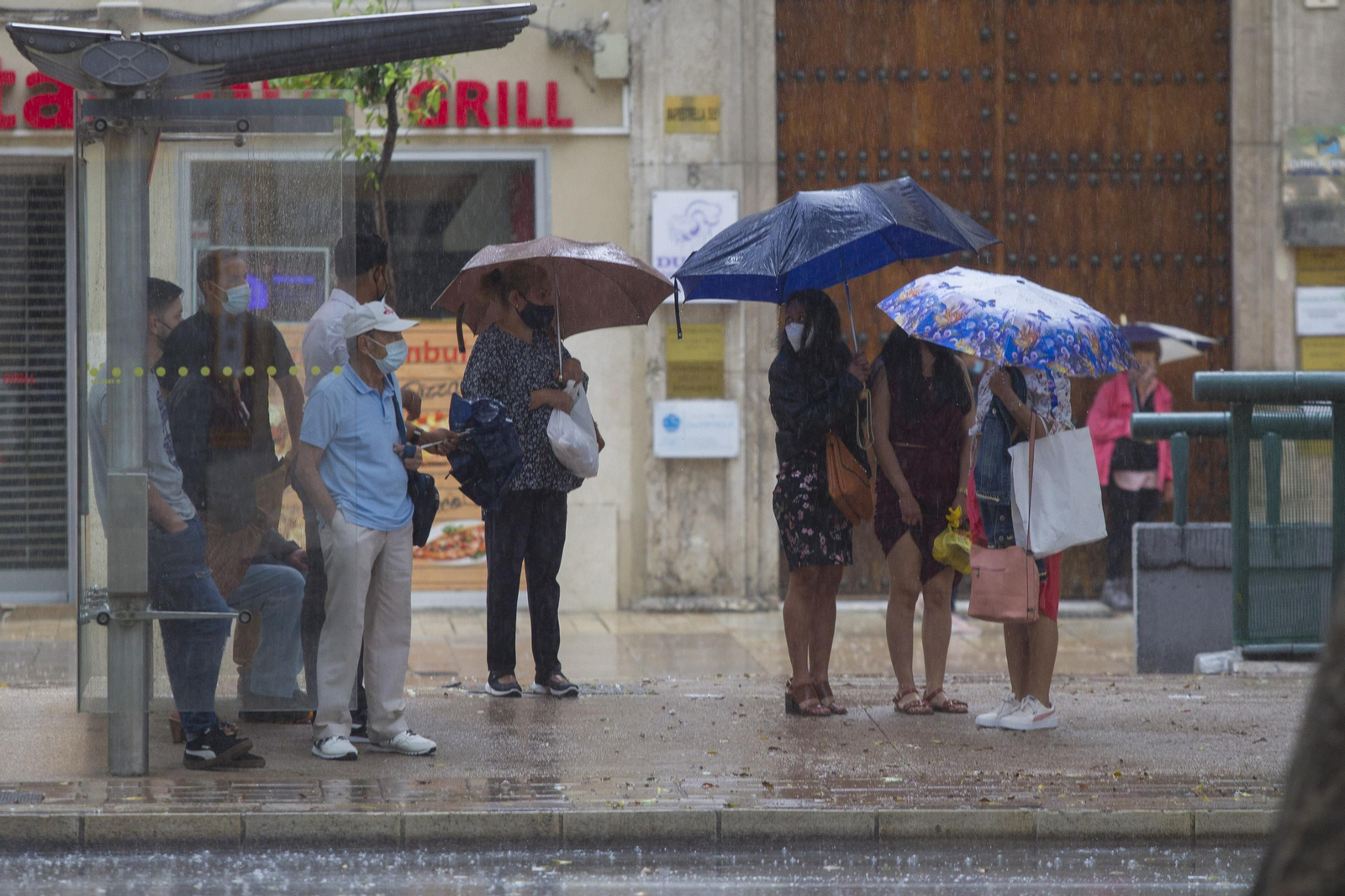 Varias personas esperan junto a una parada de autobús.