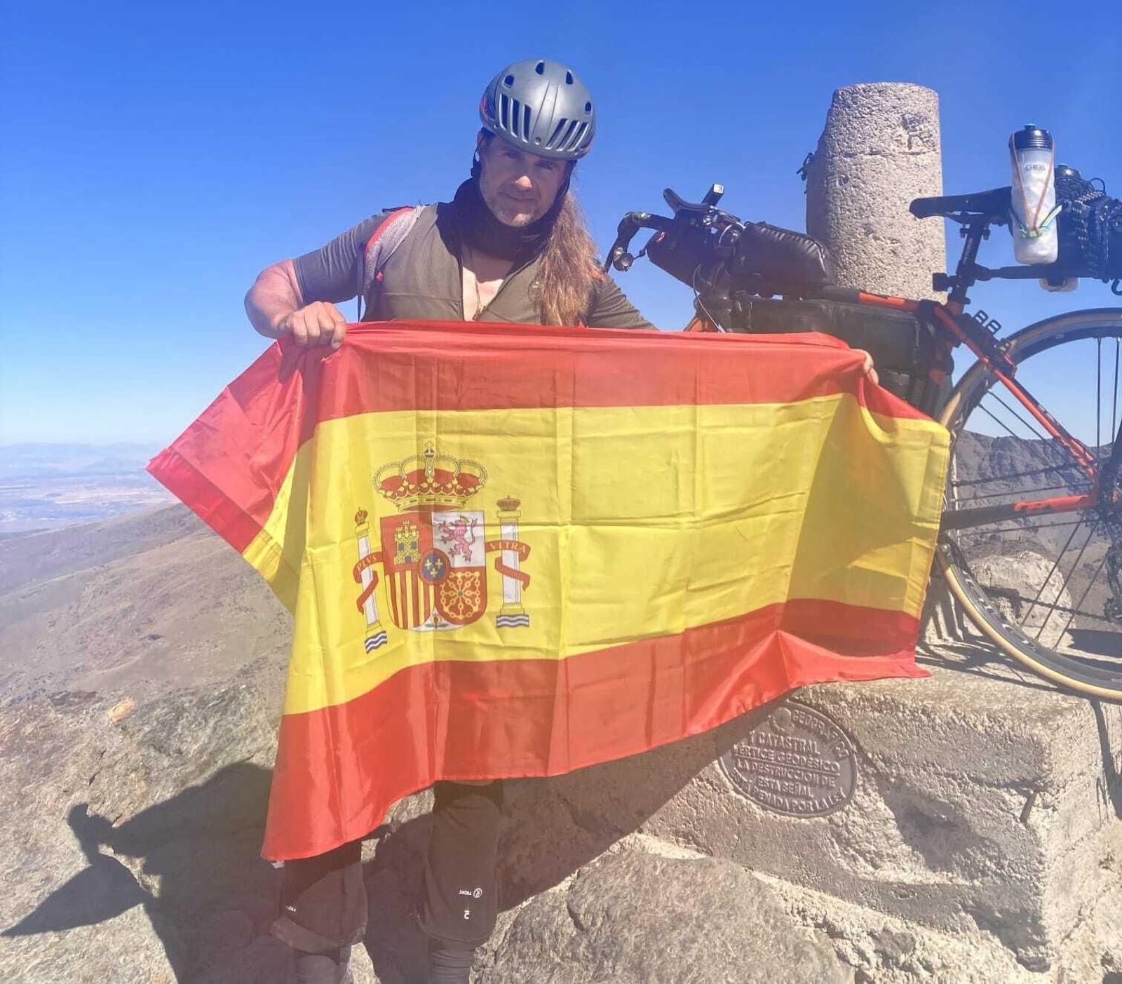 Norberto Reina posa con una bandera española y su biclicleta después de coronar una de las cimas.