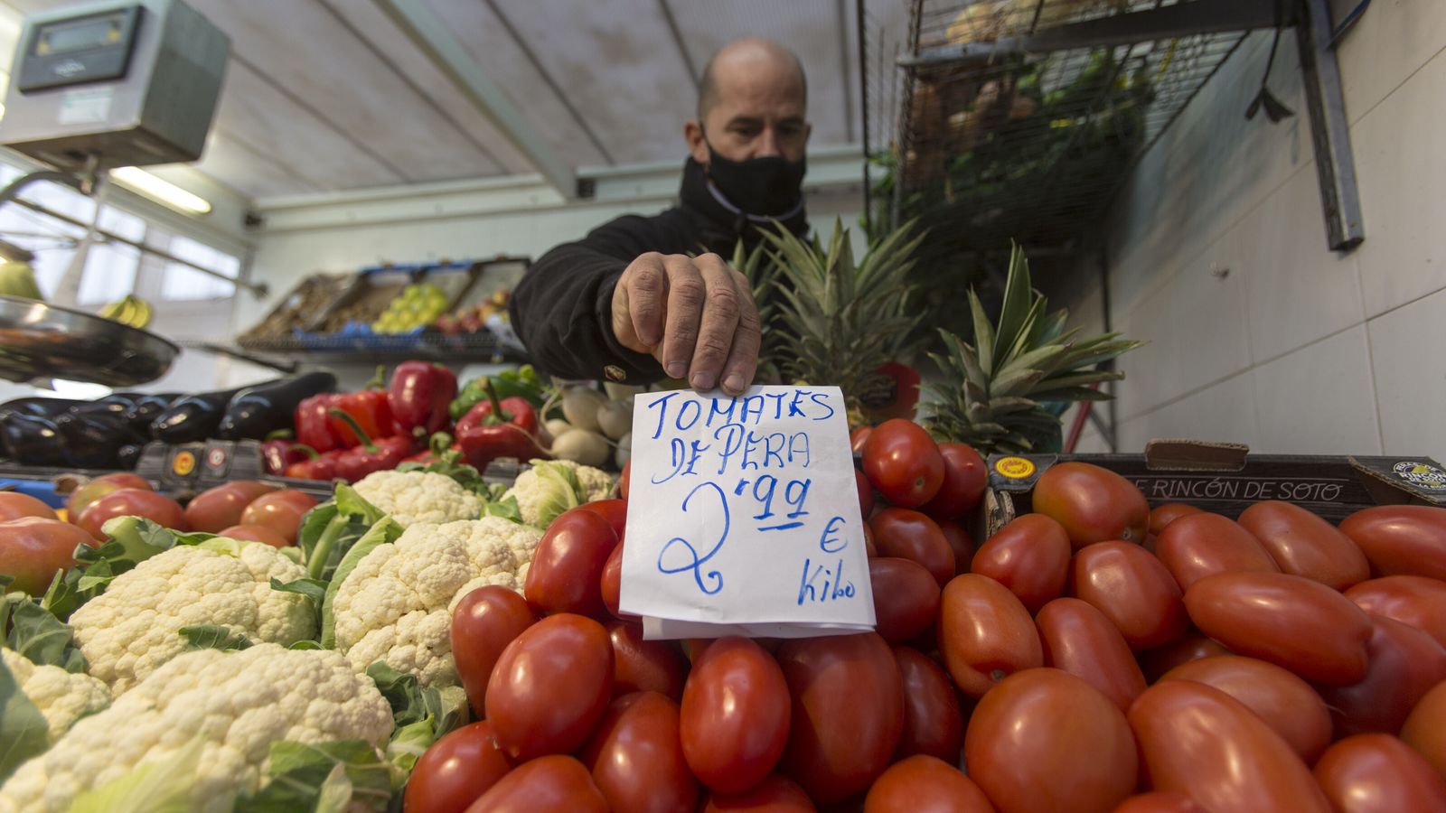 El responsable de un puesto en un mercado le pone precio a los tomates.