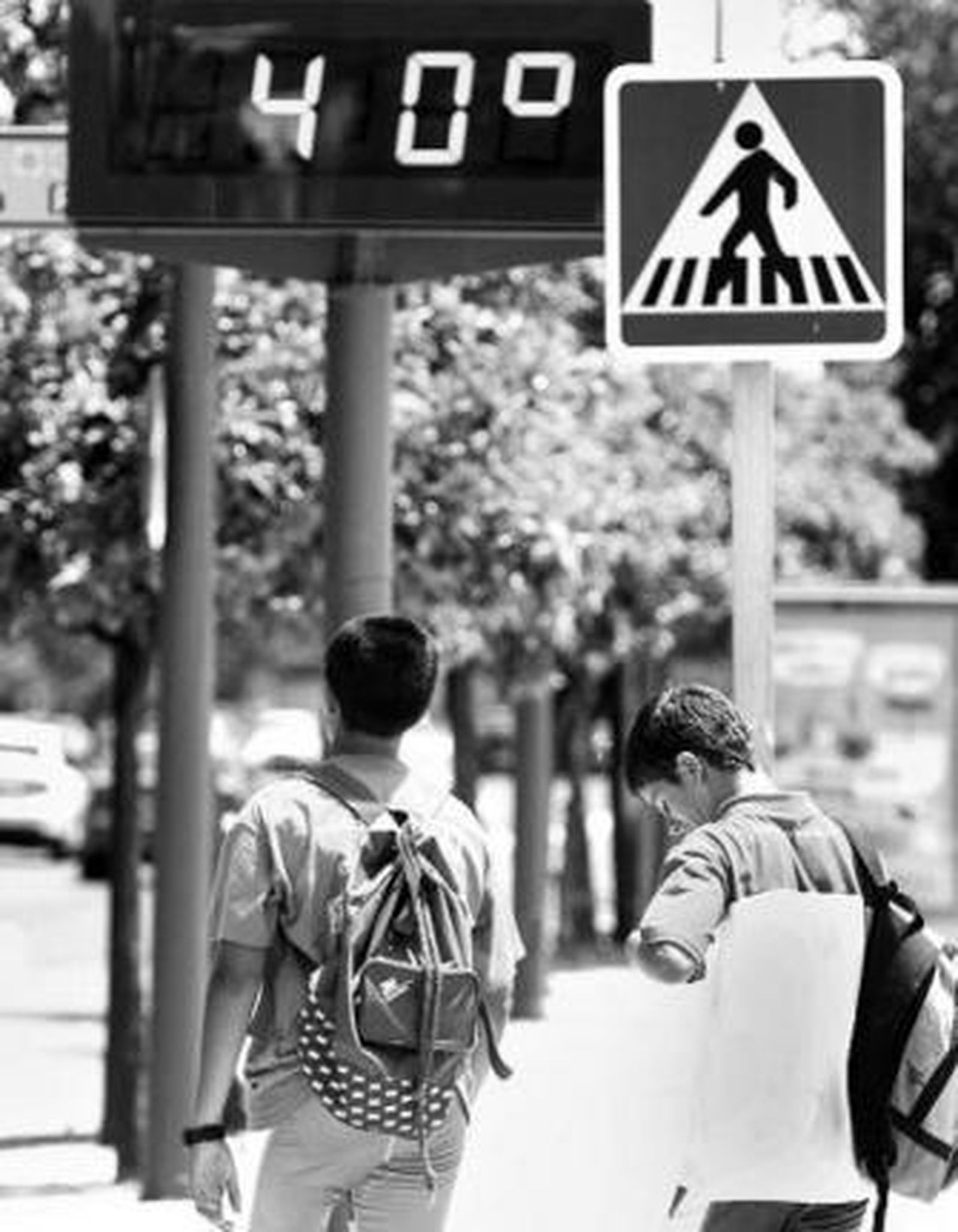 Dos jóvenes pasan bajo un termómetro que marca 40 grados.