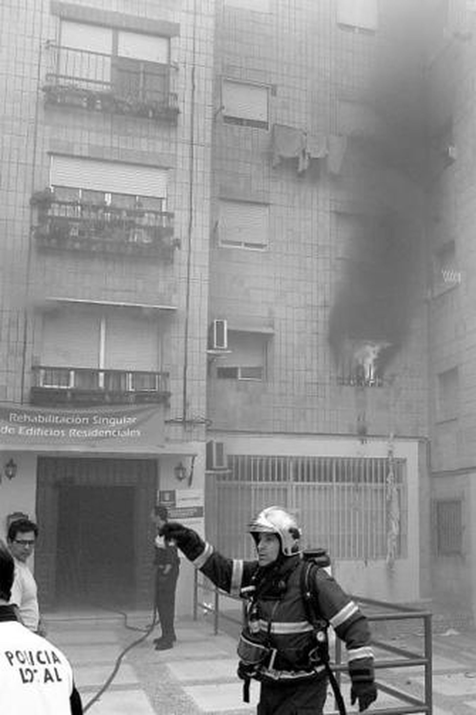 Un bombero dirige la extinción del fuego. A la dcha., la abuela afectada y el padre de las dos niñas son consolados por otros vecinos de La Granja.