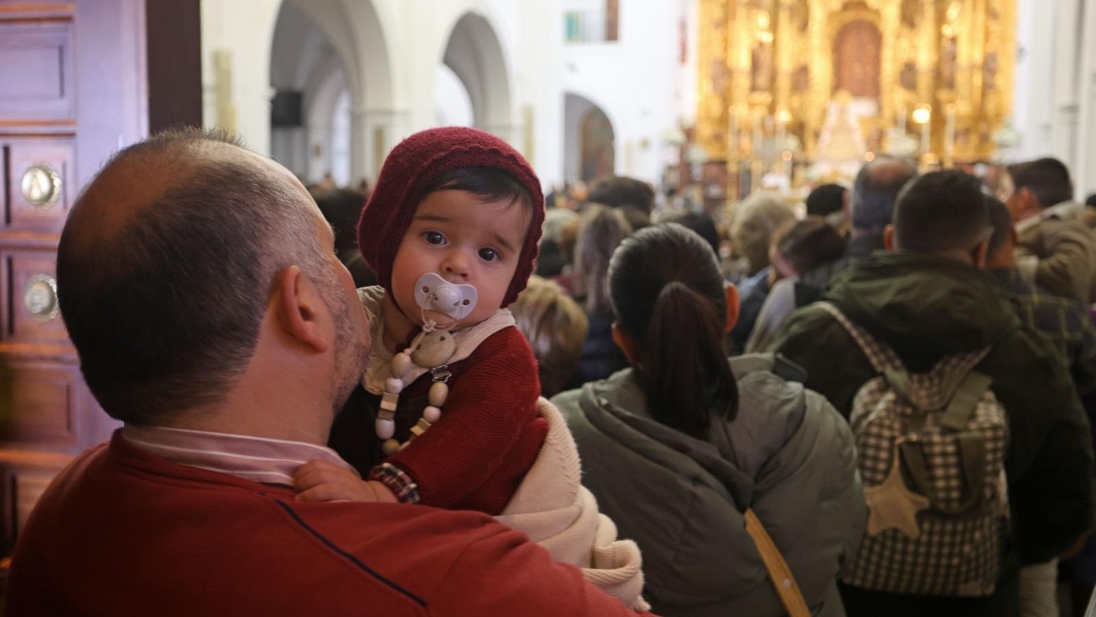 Un bebé en los brazos de su padre en la entrada a la ermita de la Virgen del Rocío.