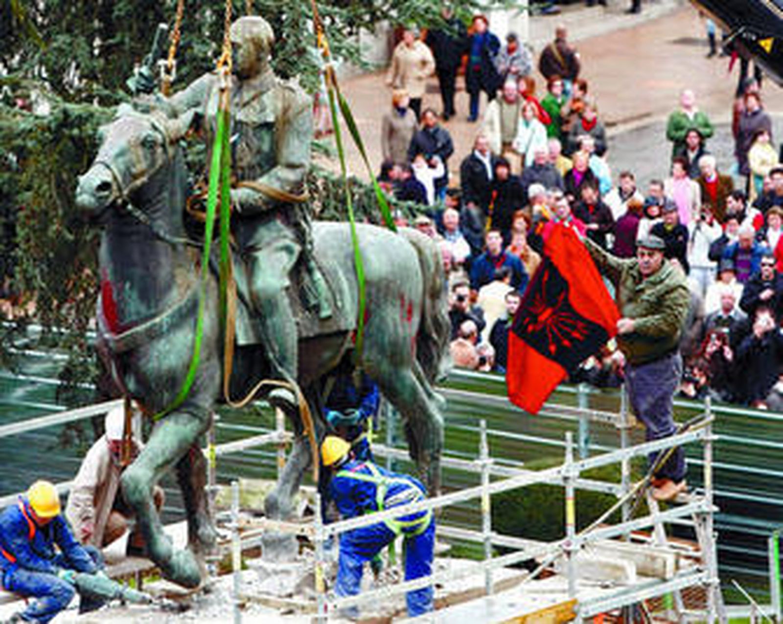 Operarios desmontan ayer la estatua de Franco ante un hombre que porta una bandera falangista.