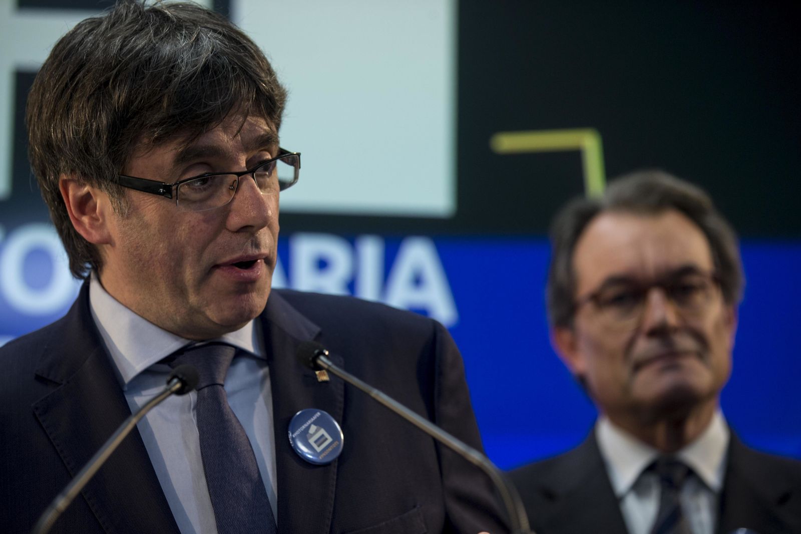 Puigdemont (i) habla con Mas al fondo.