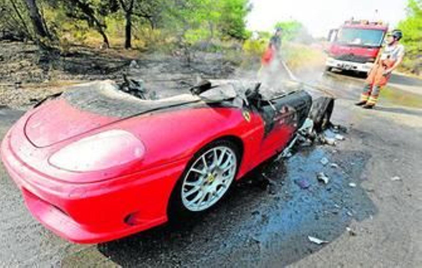 Un par de bomberos enfría los restos del Ferrari de Banega tras el incendio sufrido.
