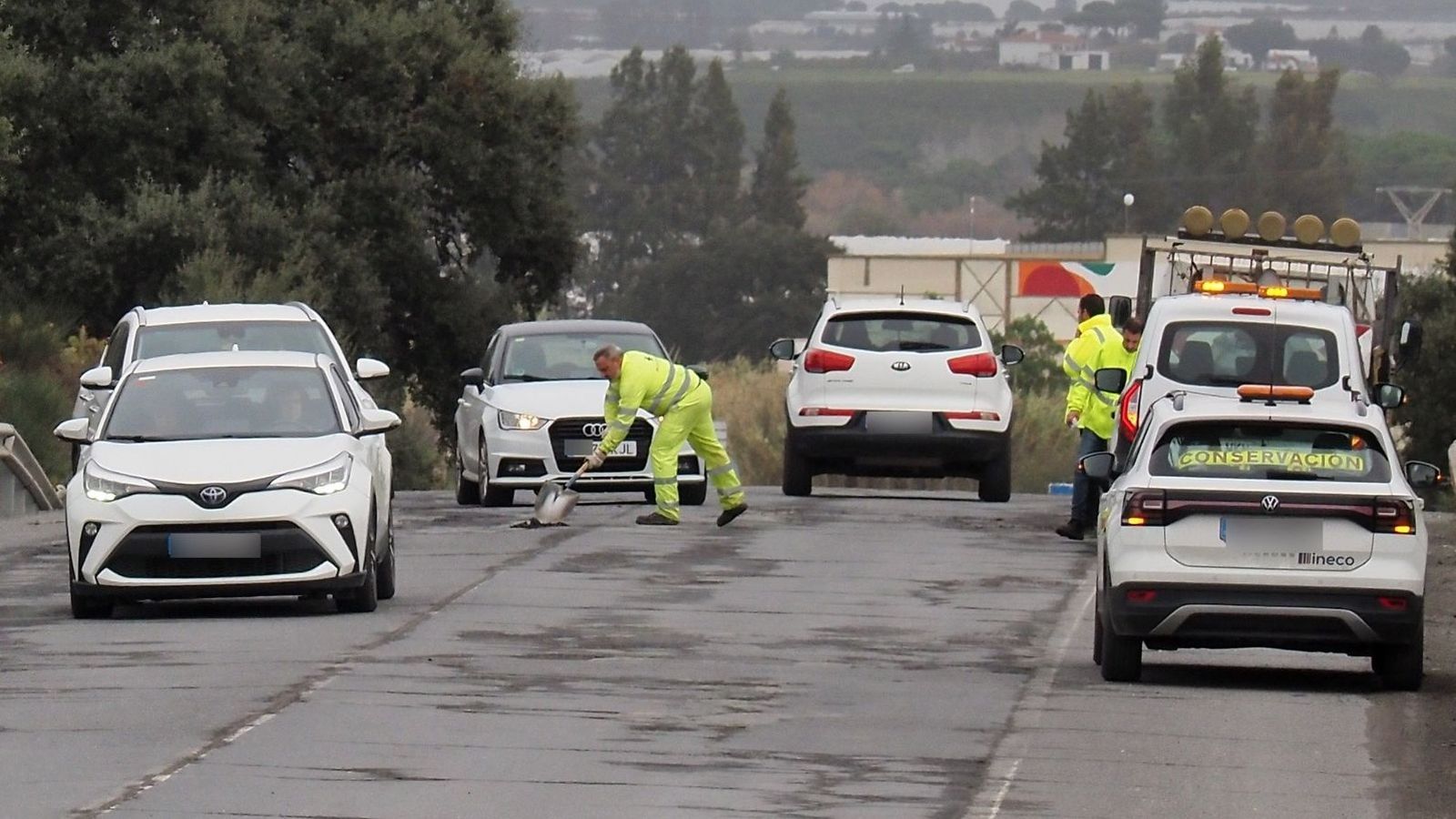 Operarios parchean la carretera rodeados de coches.